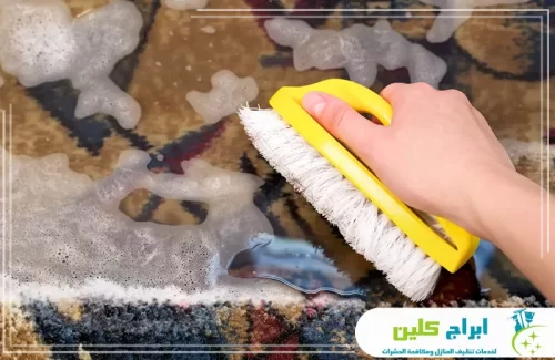 معالجة بقع السجاد بصامطة باستخدام فرش مخصصة للوصول إلى أعماق الألياف.