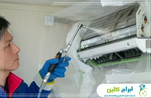 فني ينفذ غسيل مكيف سبليت بمعدات مخصصة لإزالة الأوساخ من ملفات التبريد.