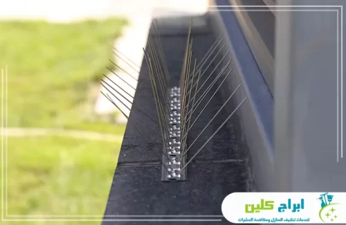 لاصق طارد الحمام بصامطة 0550234190 شركة ابراج كلين الأشواك مثبتة على حافة نافذة أو بروز جداري داكن اللون، يبدو أنه من الرخام أو الأسمنت المطلي بالأسود.