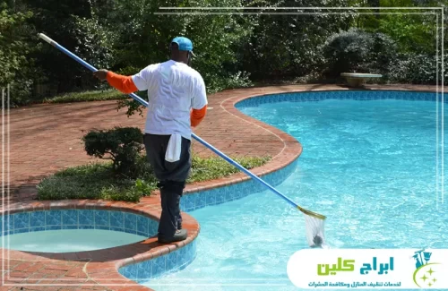 فني ينفذ تنظيف سطح المسبح وإزالة الشوائب للحفاظ على صفاء المياه.