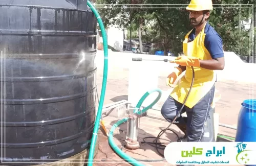 فني ينفذ تنظيف خزان مياه في بابو عريش باستخدام مضخة ضغط لإزالة الأوساخ من الخزان البلاستيكي.